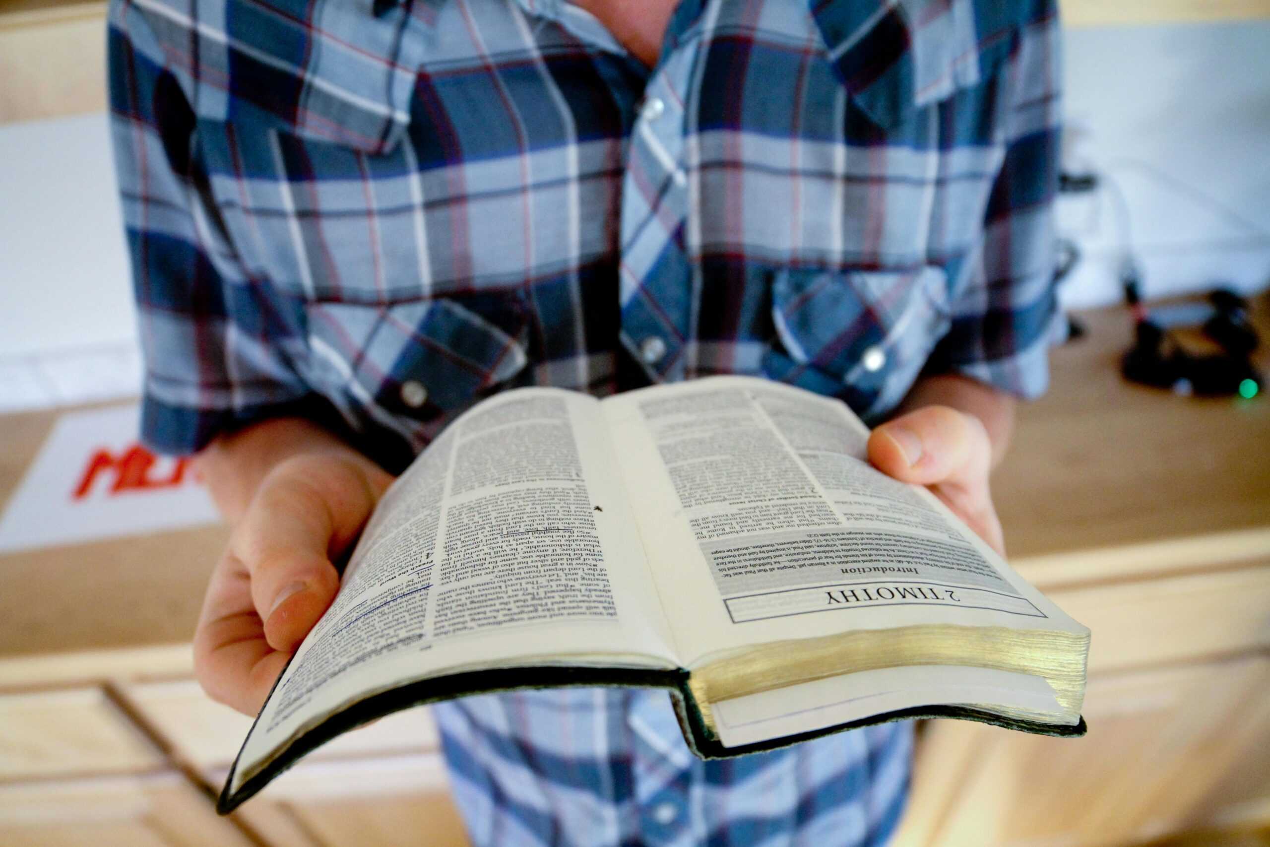 A person holding and reading an open Bible, focusing on the book of Timothy.