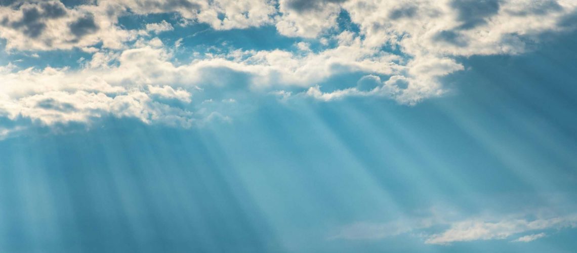 Vibrant sunrays pierce through a cloudy sky, creating a dramatic and dreamy cloudscape.