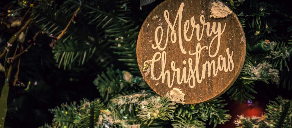 Close-up of a Merry Christmas ornament on a decorated fir tree, evoking festive holiday spirit.