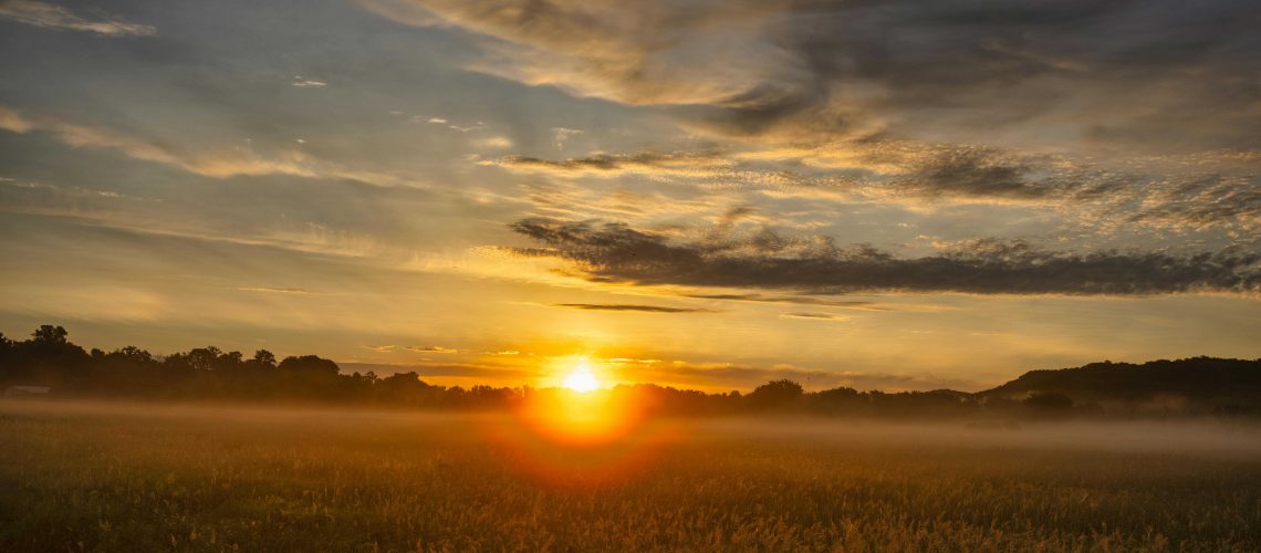 Dramatic sunrise with golden hues over a misty rural landscape in Modena, WI.