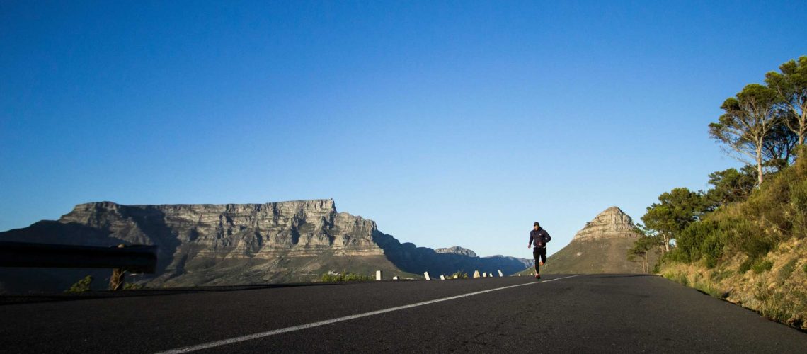 Man jogging along a scenic road with Table Mountain view in Cape Town.