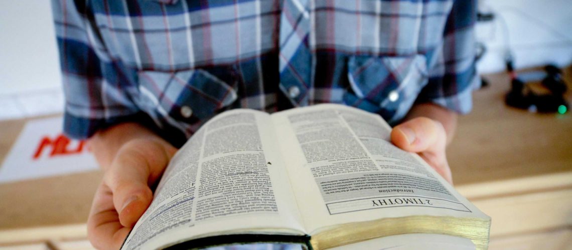 A person holding and reading an open Bible, focusing on the book of Timothy.