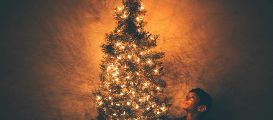 A child smiles at a beautifully lit Christmas tree highlighting the festive glow.