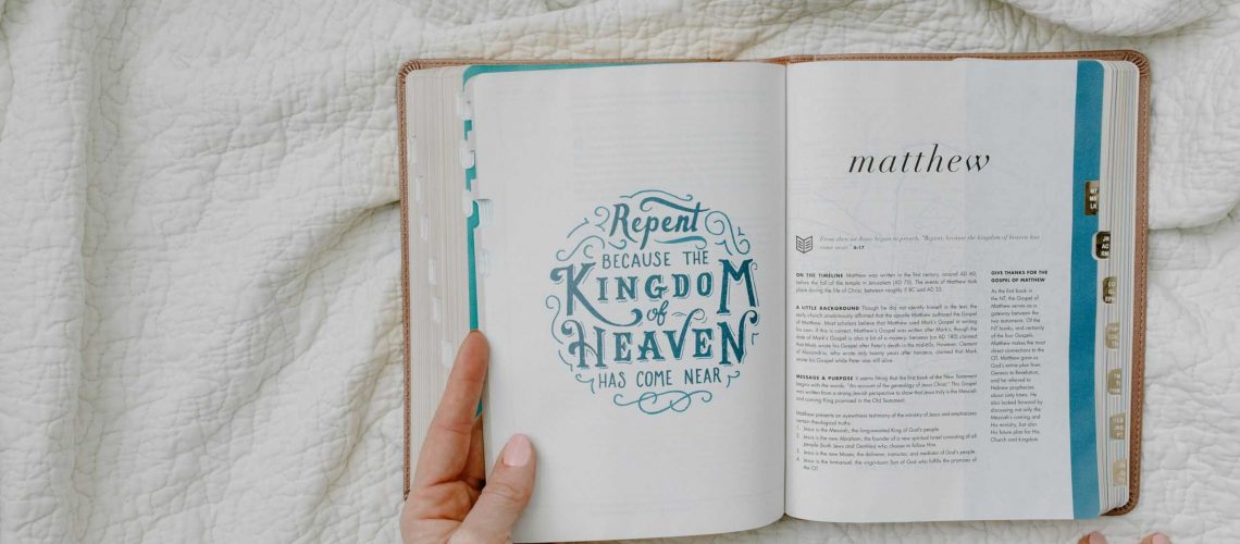 Open Bible with focus on Matthew passage and text 'Repent'. Hands showing, resting on a quilt.