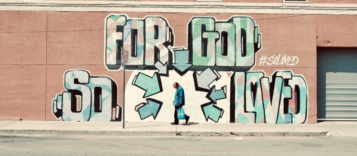 A man walks beside a large street art mural with graffiti text on a city wall, creating a vibrant urban scene.